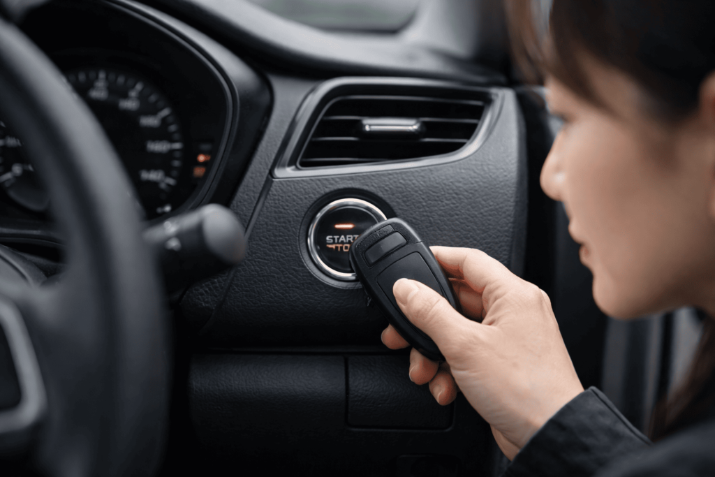 スマートキーをスタートボタンに直接当てて緊急始動を試す日本人女性の車内手元アップ