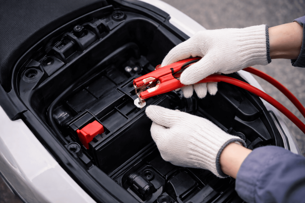 スクーターのバッテリーにジャンプケーブルのプラス端子を接続する様子