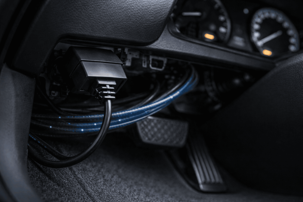 運転席下のOBD2接続部を写し、外部機器の常時接続による通信負荷をイメージさせる写真
