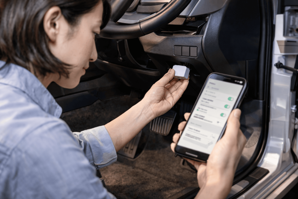 日本人女性が車内でOBD2アダプタを接続し、スマホで設定変更を行っているイメージ